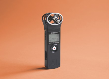 Image of a Zoom H1 black audio recorder standing upright with an orange coloured background